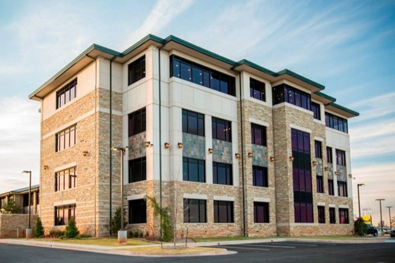 Exterior view of Frontier State Bank in Oklahoma City, OK — a modern four-story commercial building with stone and stucco façade, large tinted windows, and a flat roofline, captured during golden hour under a blue sky.